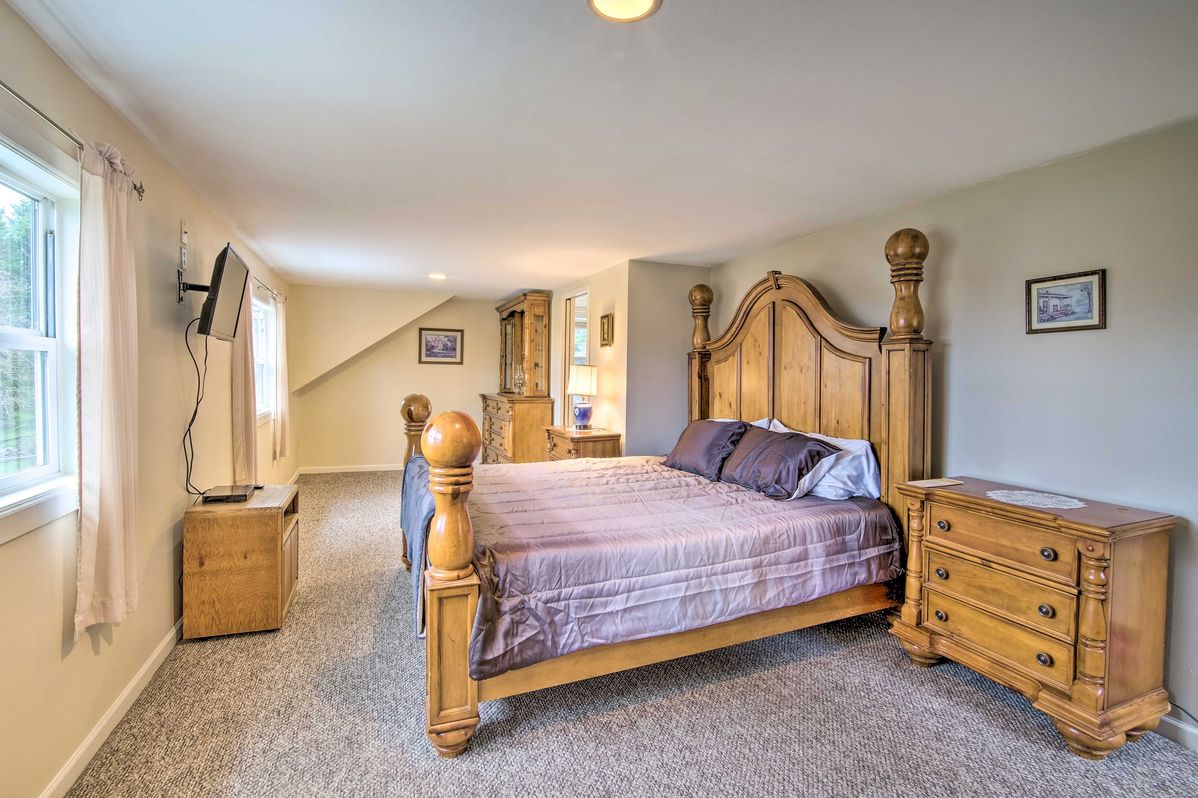 A bedroom with a wooden four-poster bed, a nightstand, a dresser, and a television mounted on the wall.