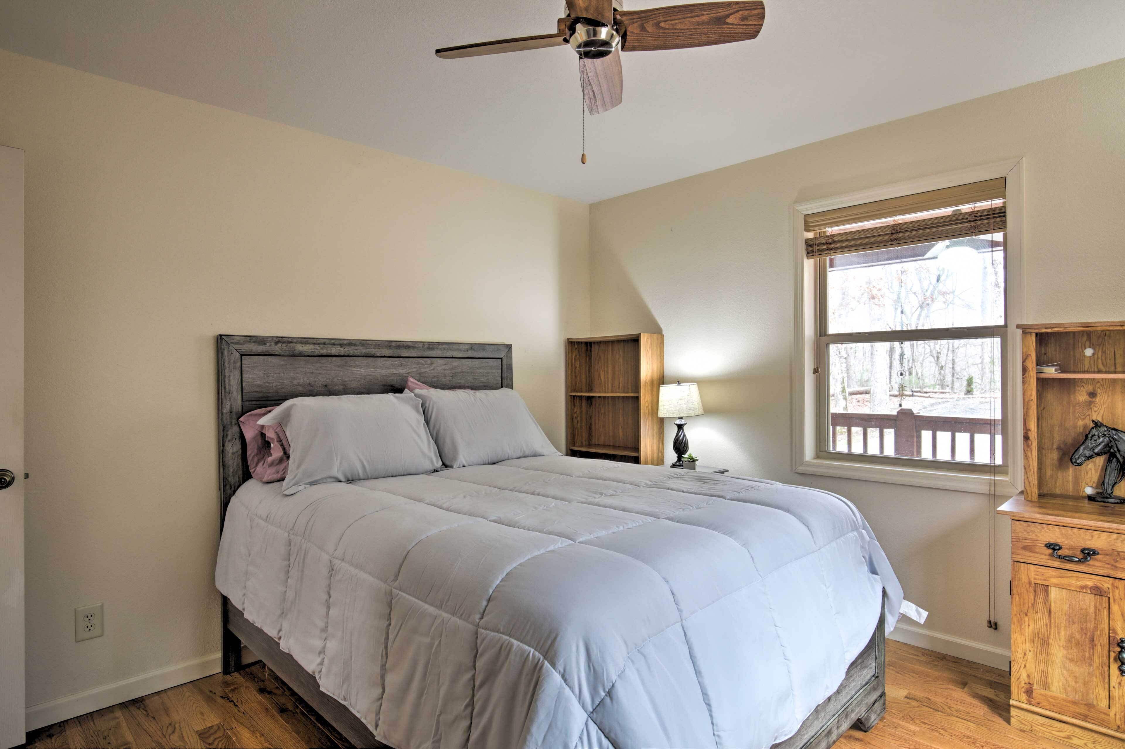 A bedroom with a bed, a ceiling fan, a window with blinds, a nightstand, and a wooden cabinet.