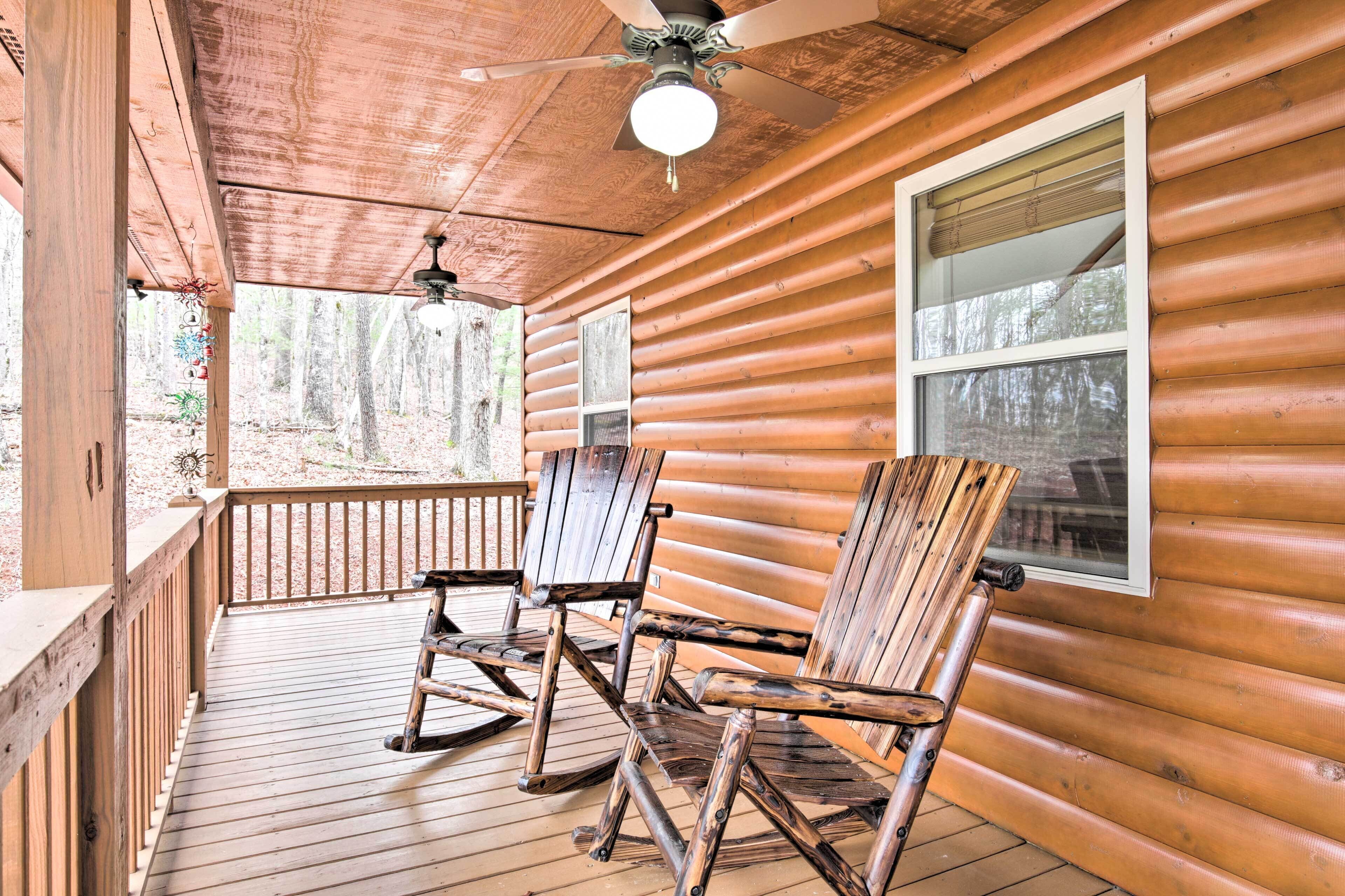 A wooden cabin with a porch, rocking chairs, and a ceiling fan.