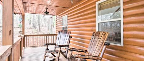 A wooden cabin with a porch, rocking chairs, and a ceiling fan.