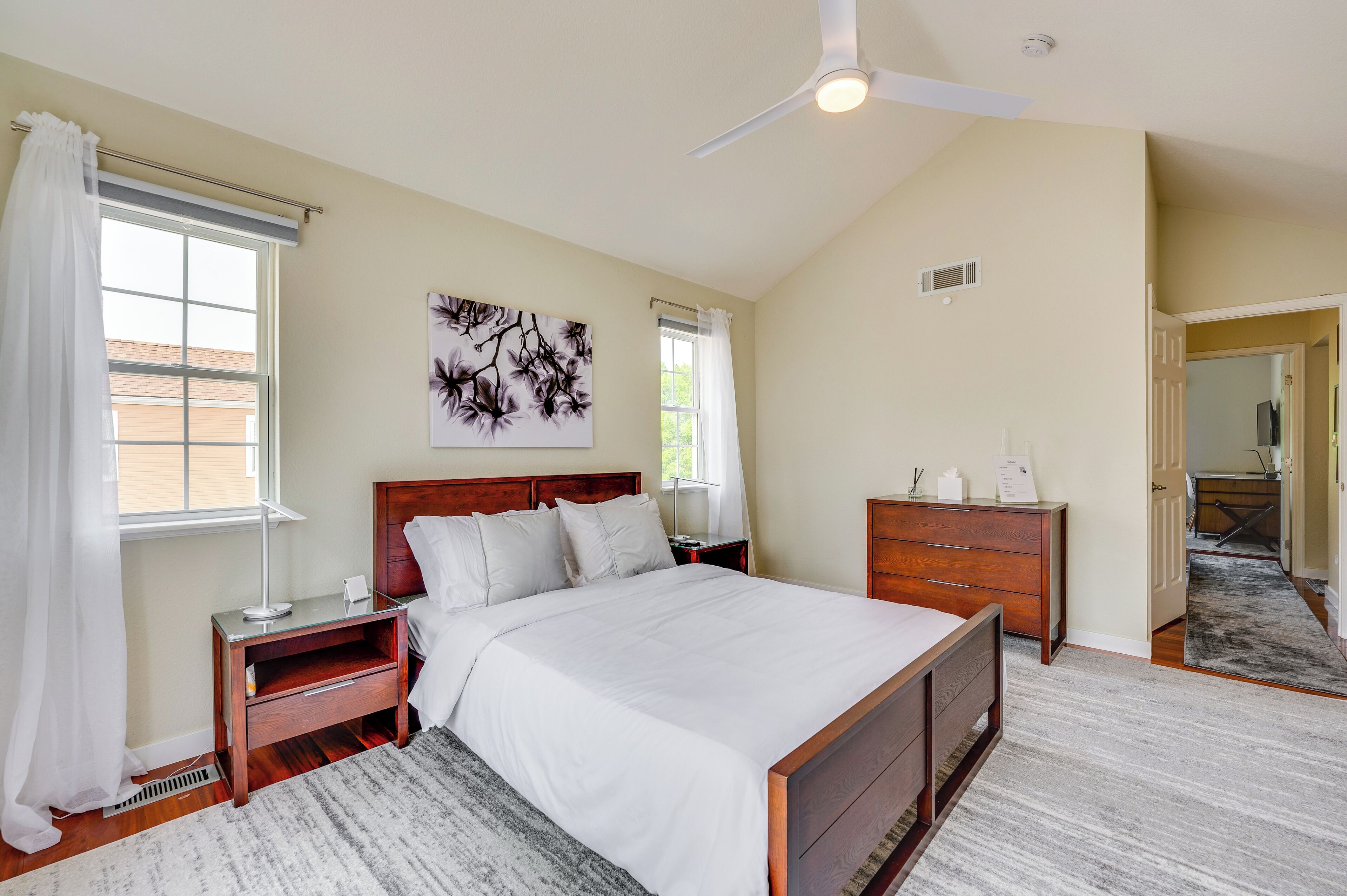 A bedroom with a large bed, a nightstand, a dresser, a ceiling fan, and a window with curtains.