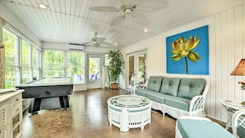A spacious room with a pool table, a green sofa, a white wicker chair, and a ceiling fan.