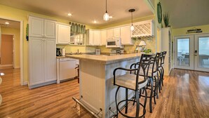 A kitchen with white cabinets, a central island with bar stools, a microwave, and a hanging light fixture. - Kentucky Lake House With a Great Outdoor Space! (Gilbertsville)