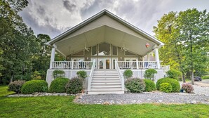 A two-story building with a covered porch, a staircase leading to the entrance, and a well-maintained garden with hedges and trees. - Kentucky Lake House With a Great Outdoor Space! (Gilbertsville)