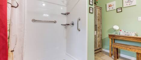 A shower with a glass door, a wooden bench, and a small table with a mirror and toiletries.