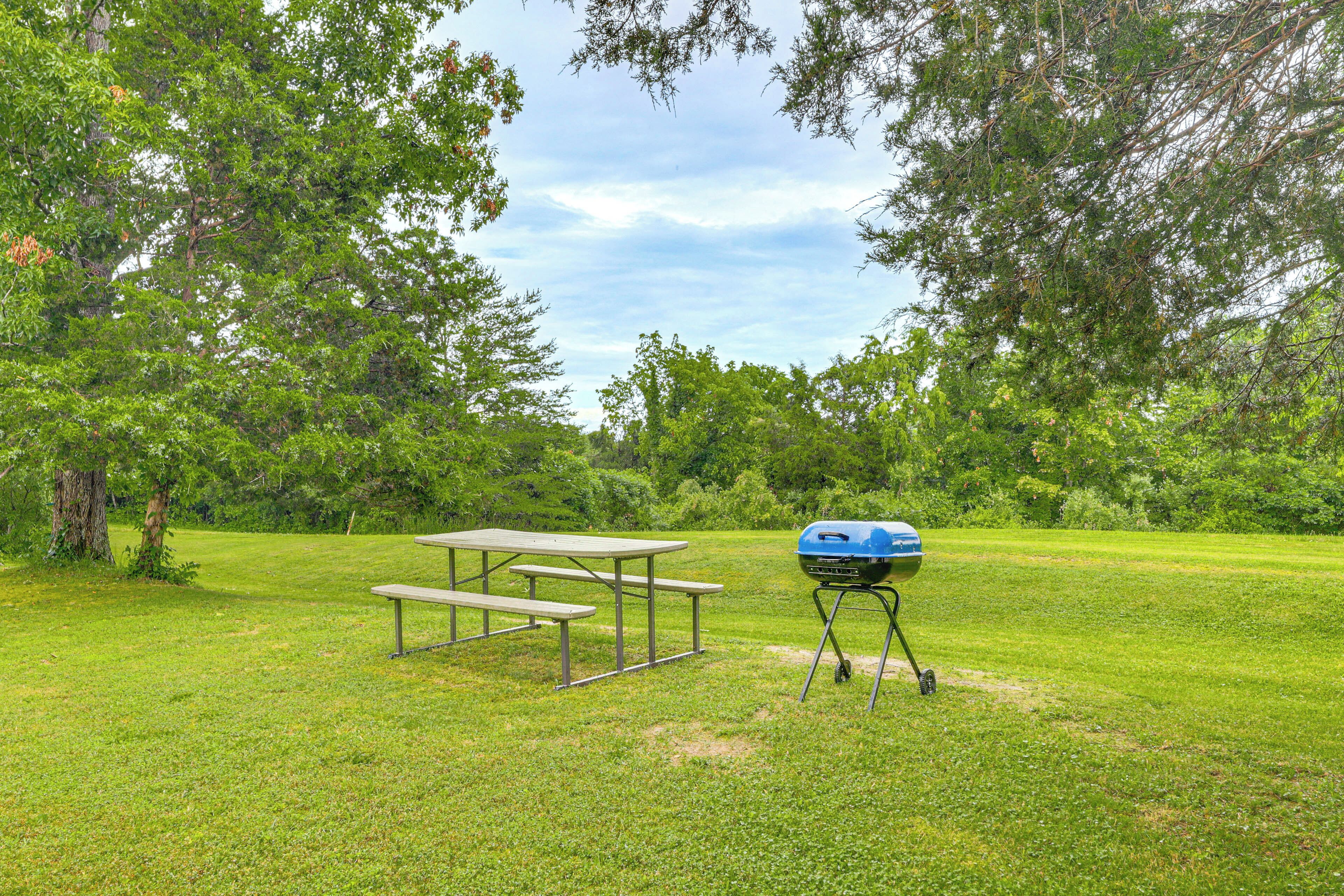 Ein Picknickbereich mit Grill und Bänken in einem grünen Park.