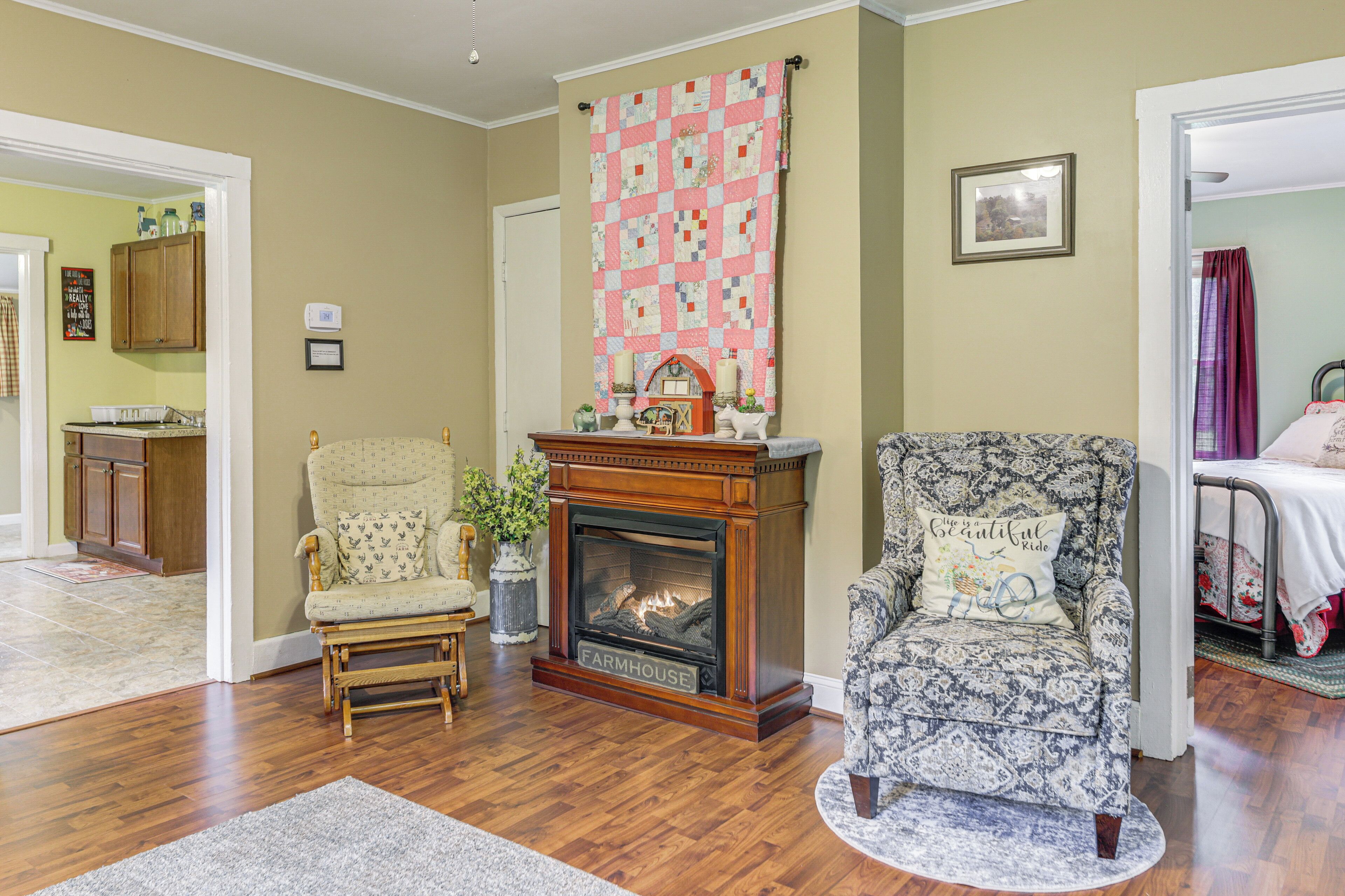 A living room with a fireplace, two armchairs, a rug, and a quilt hanging on the wall.