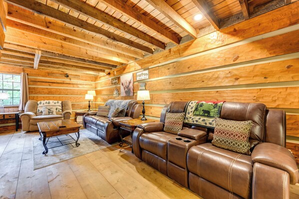 A log cabin interior with a leather sofa, a wooden coffee table, and a fireplace. - Fire Pit + Yard Games: Cosby Cabin Hideaway! (Cosby)