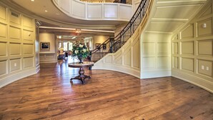 A spacious foyer with a grand staircase, polished wooden floors, and a central floral arrangement. - Walk to Pier & Golf: Heart of Harbour Town Condo (Hilton Head Island)