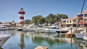 A marina with boats docked, a lighthouse, and buildings with balconies. - Walk to Pier & Golf: Heart of Harbour Town Condo (Hilton Head Island)
