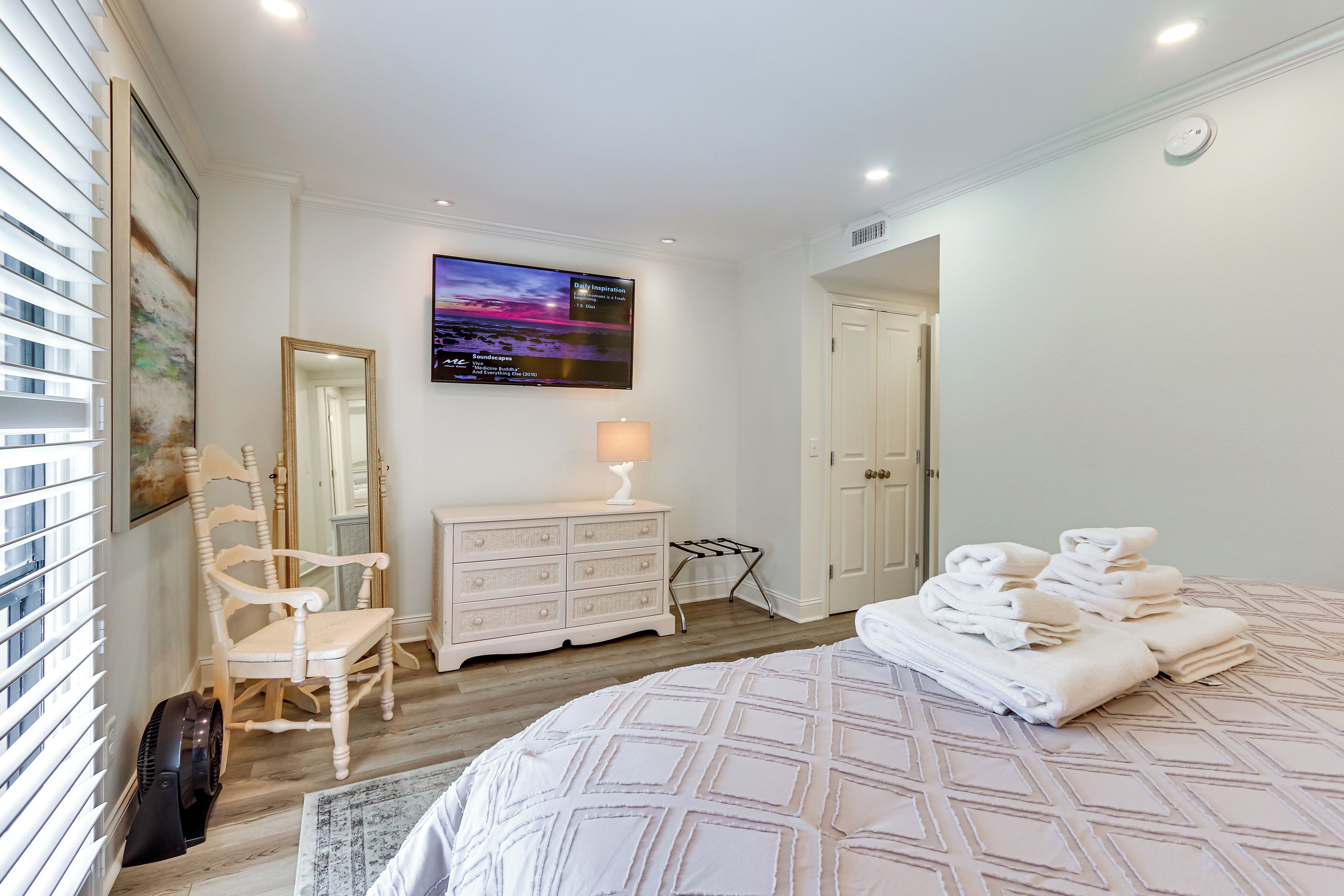 A bedroom with a bed, a dresser, a chair, a TV, and a door.