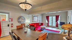 A spacious living room with a wooden dining table, red sofa, and a large wall clock.