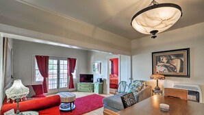 A spacious living room with a wooden dining table, red and grey sofas, a red rug, and a chandelier.