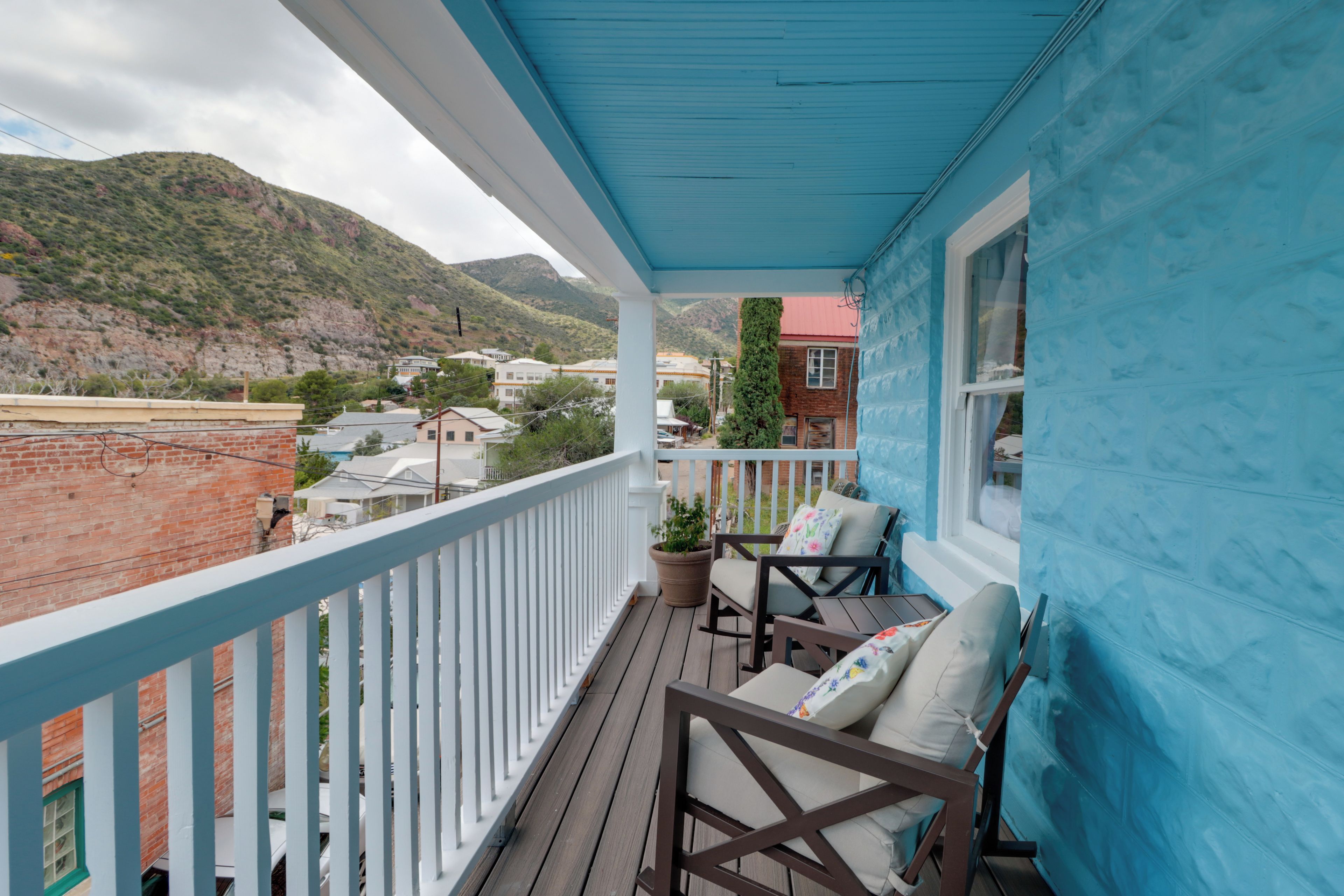 A balcony with a view of a mountainous landscape, a brick building, and a clear sky.