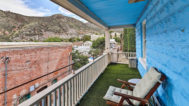 A balcony with a blue awning, a small grassy area, and a white cushioned chair.