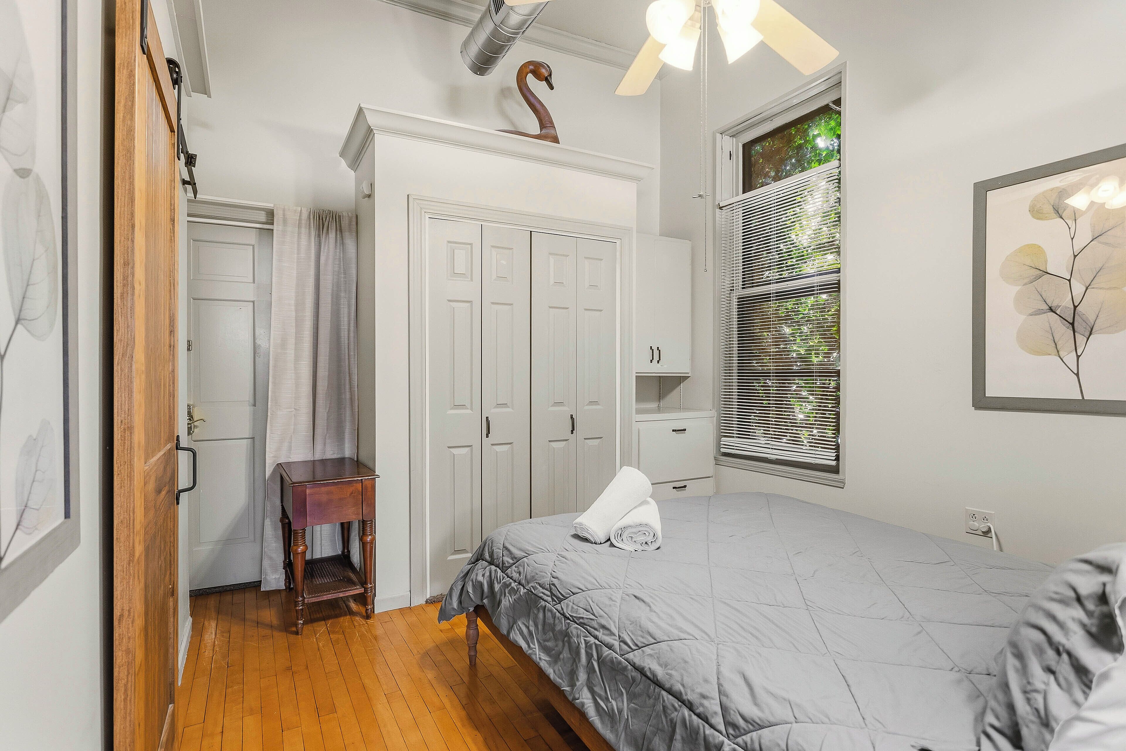 Un dormitorio con cama, armario, una mesita y una ventana con persianas.