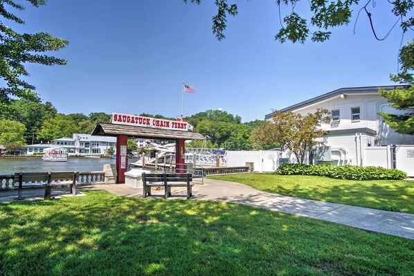 A waterfront park with a sign for 'Saugatuck Chain Ferry' and a boat docked in the background.