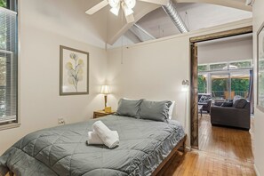 Une chambre à coucher comprenant un lit, une lampe de chevet, une œuvre d’art encadrée et donnant sur un espace extérieur aménagé avec des sièges.