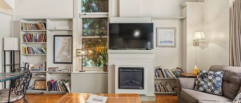 Een woonkamer met een open haard, boekenkasten, een televisie en een bank.