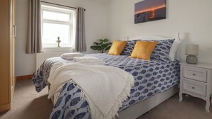 A bedroom with a bed, a bedside table, a nightstand, a window with curtains, and a wall-mounted picture.