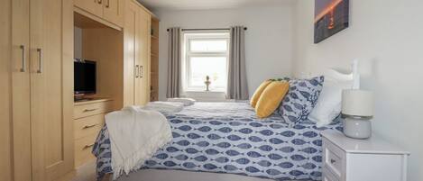 A bedroom with a bed, a TV, a desk, and a wardrobe.