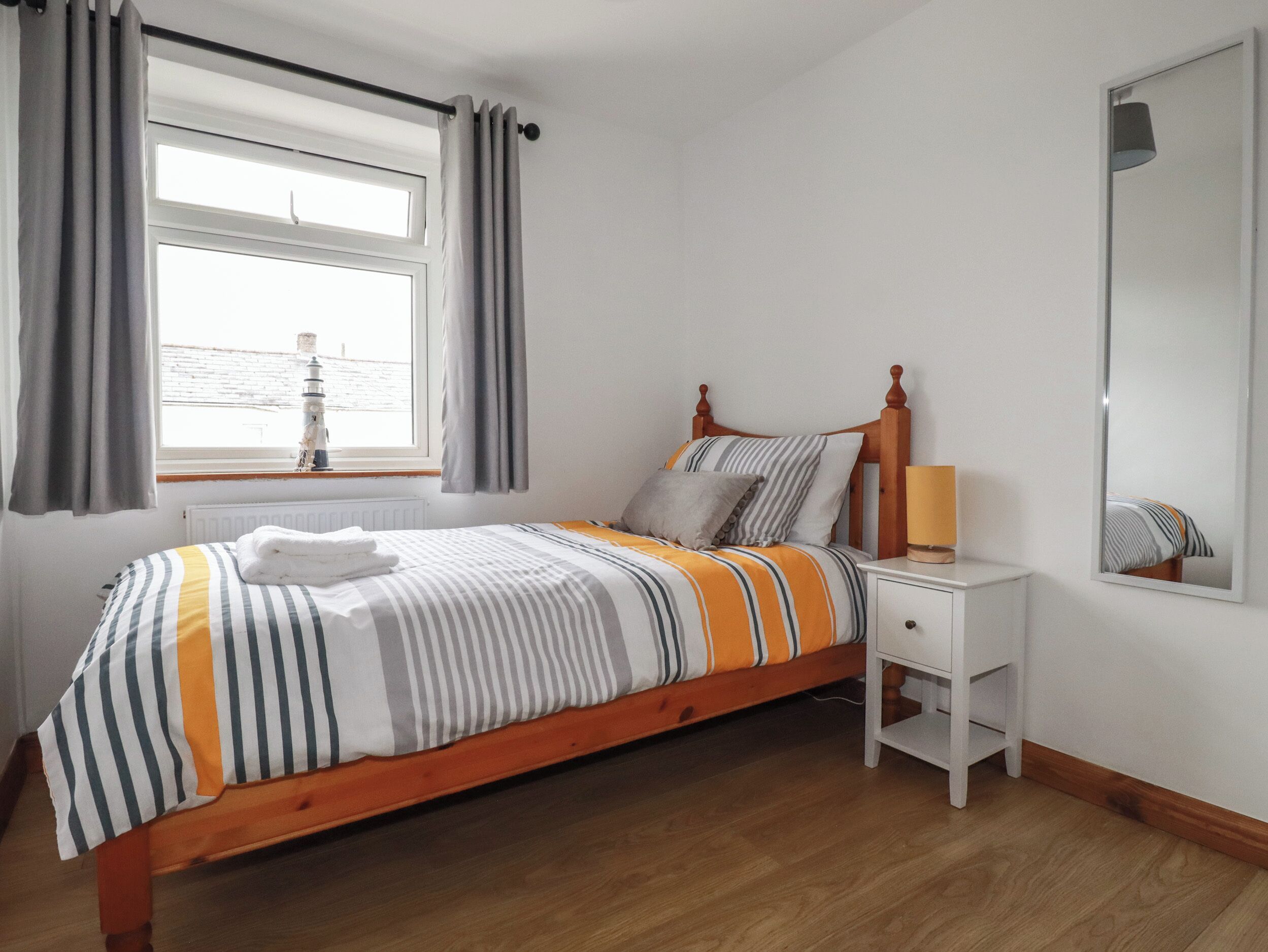 A neatly made bed with striped bedding, a bedside table with a lamp, and a window with curtains.