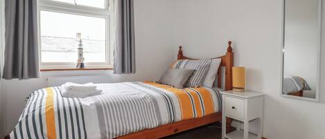 A neatly made bed with striped bedding, a bedside table with a lamp, and a window with curtains.