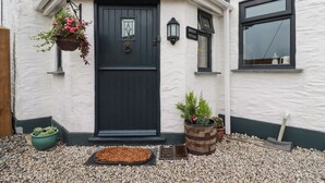 A cottage with a dark blue door, white exterior walls, and a small window. There are flower pots and a doormat in front of the door.