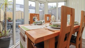 A conservatory with a dining table set for four, surrounded by wooden chairs.