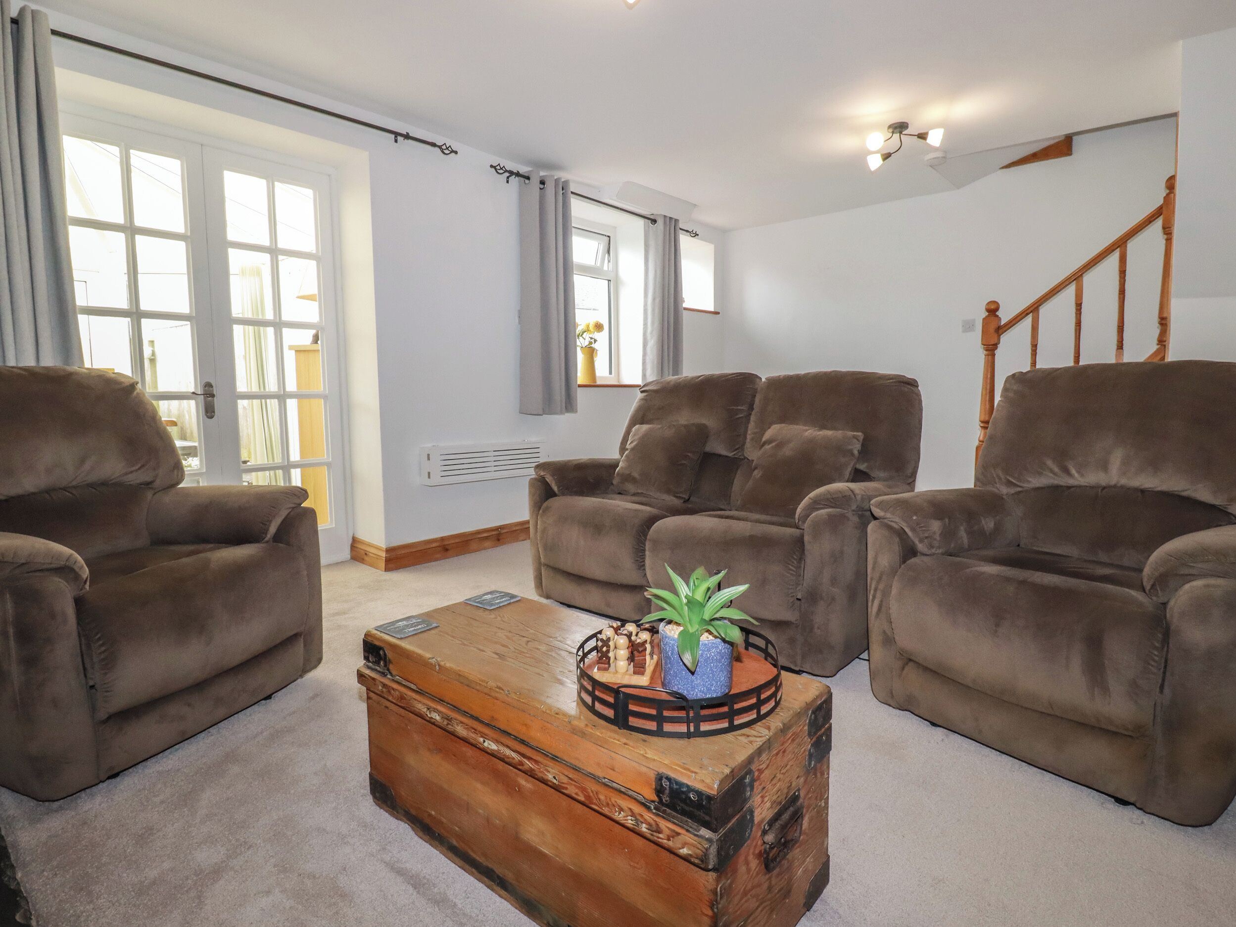 A living room with three brown sofas, a wooden coffee table with a plant, and a staircase in the background.