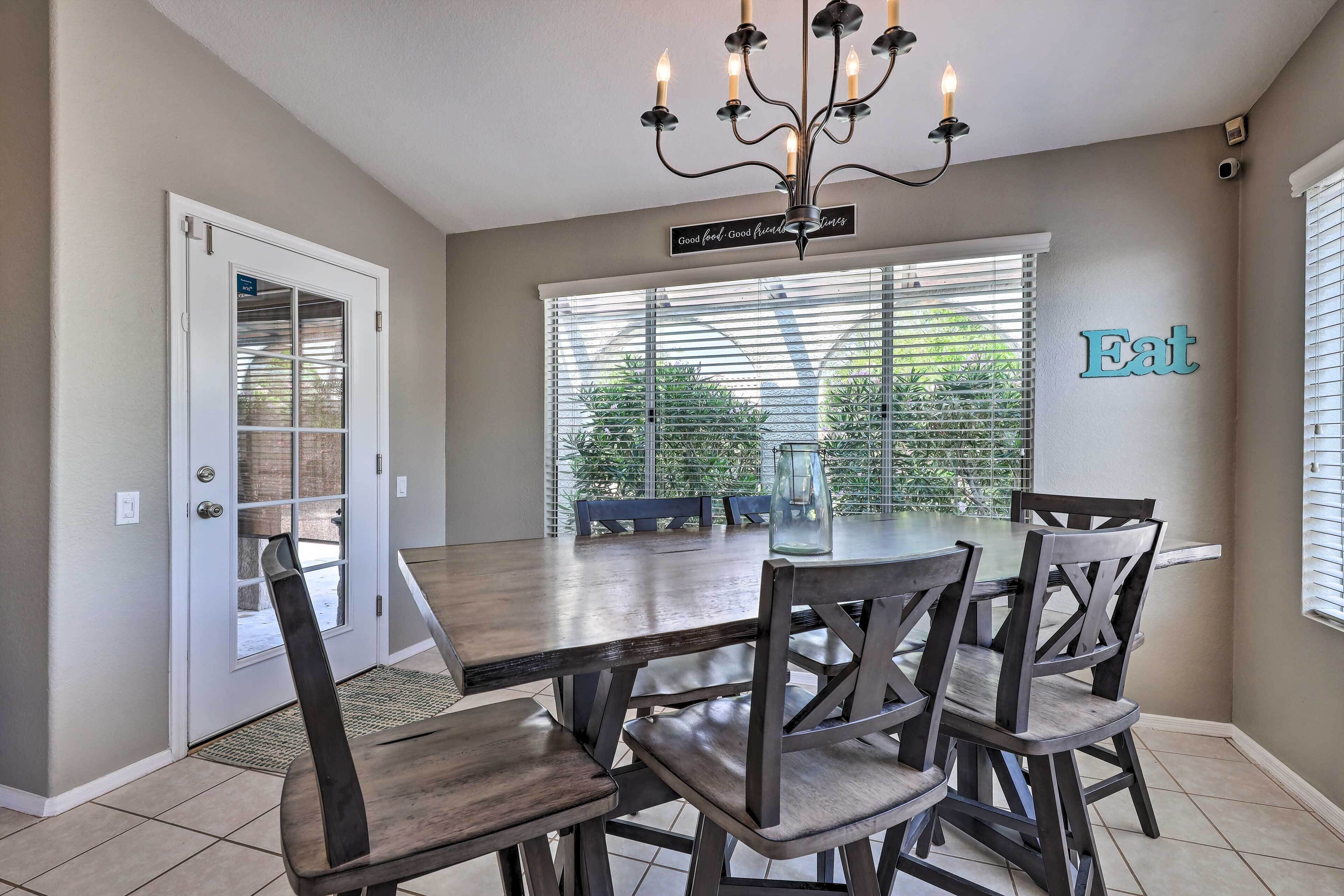 A dining area with a wooden table and chairs, a chandelier, and a sign that reads "Good food, Good friends."