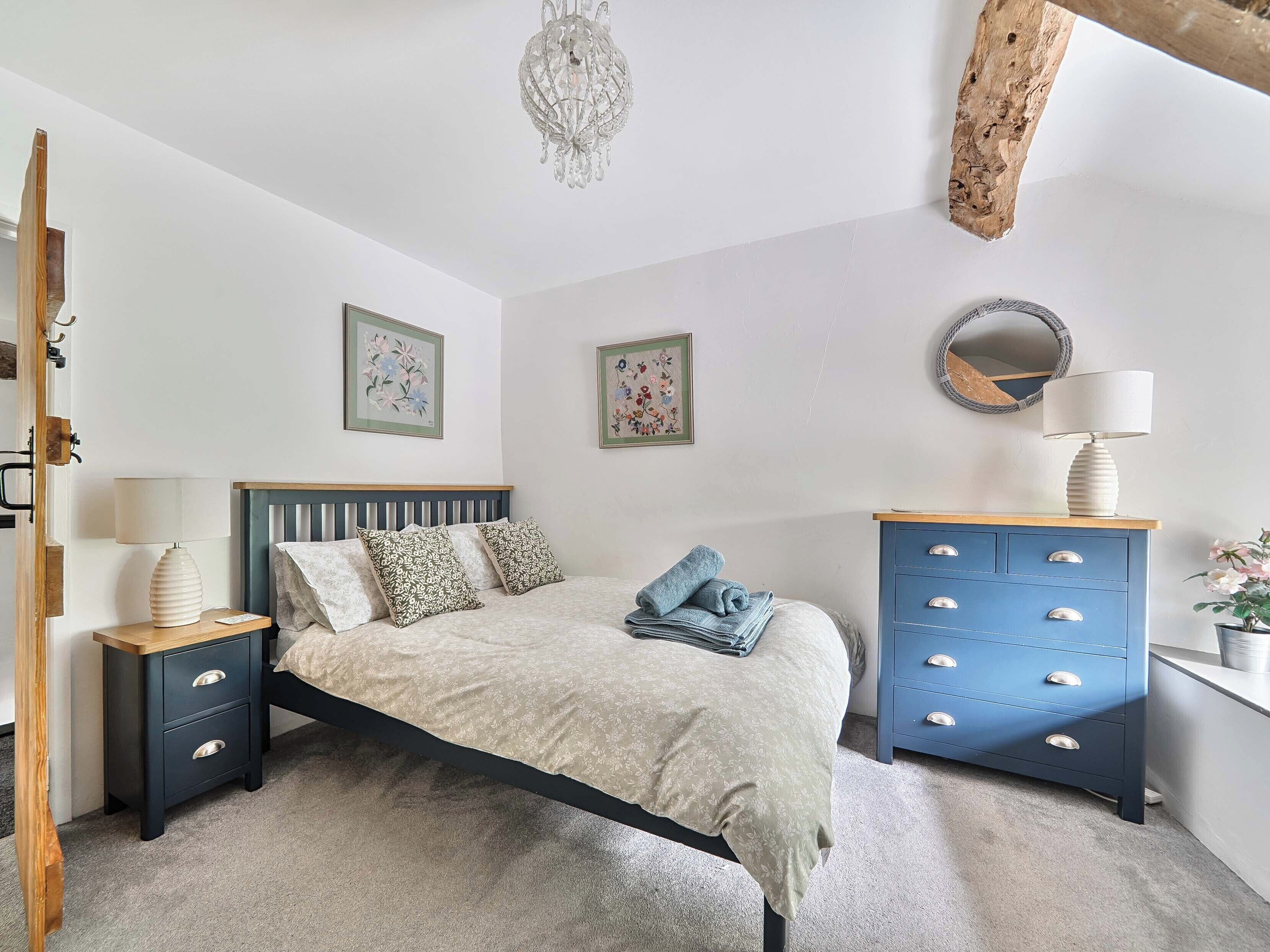 A bedroom with a bed, a dresser, a nightstand, a chandelier, and wall art.