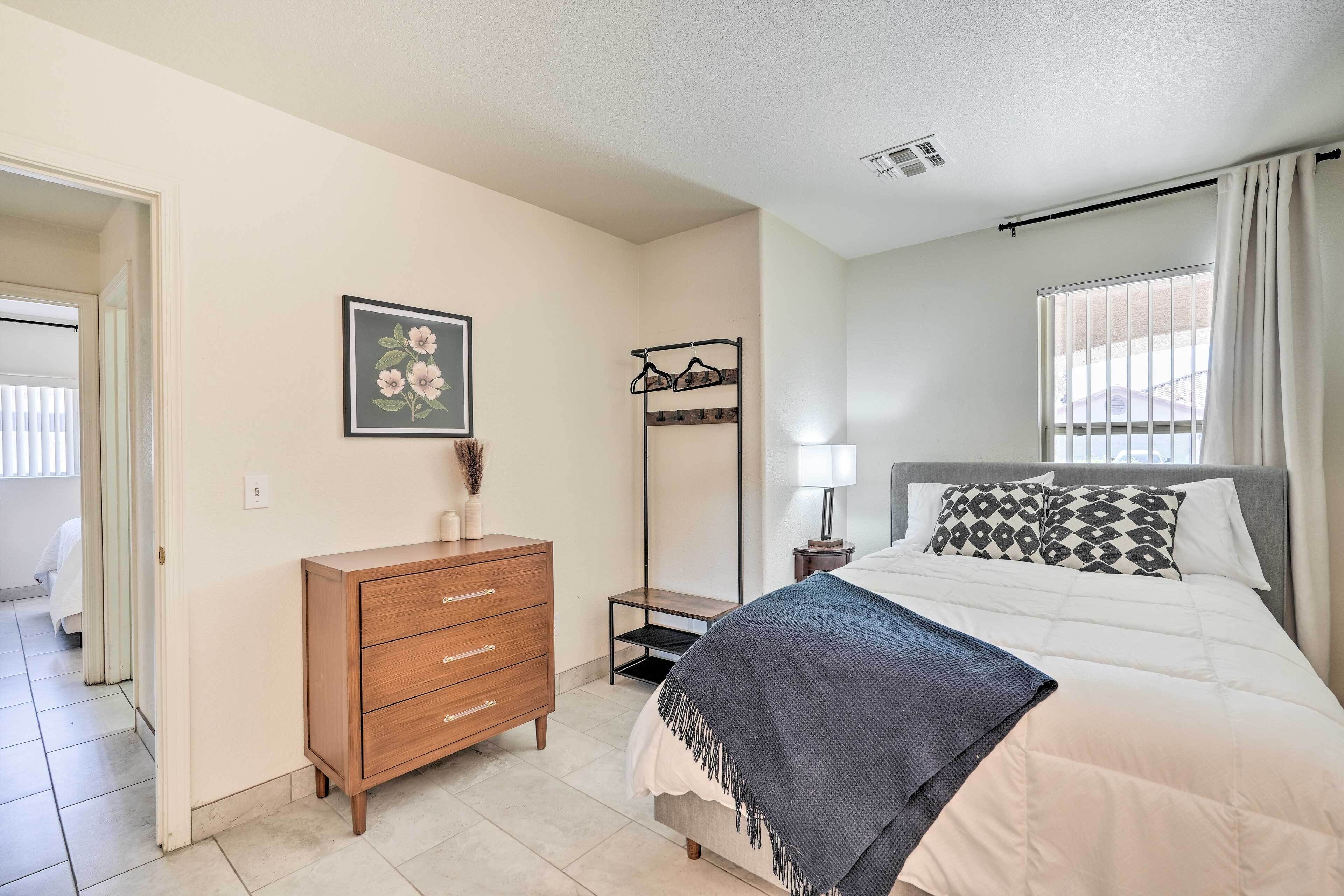 Quarto com cama, penteadeira, mesa de cabeceira, abajur e janela com cortinas.