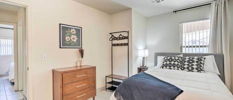 Quarto com cama, penteadeira, mesa de cabeceira, abajur e janela com cortinas.