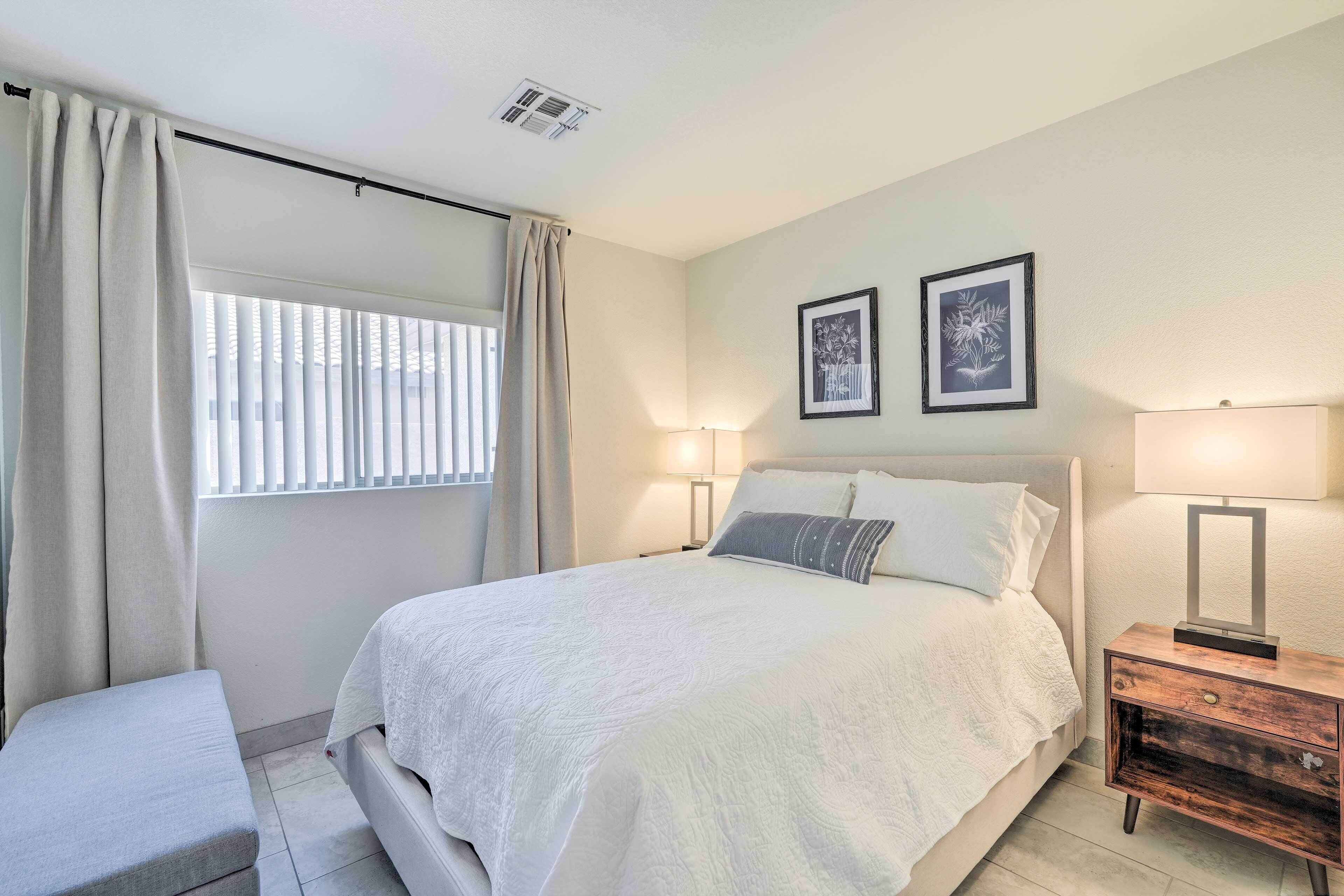 A bedroom with a bed, bedside tables, a bench, and a window with curtains.