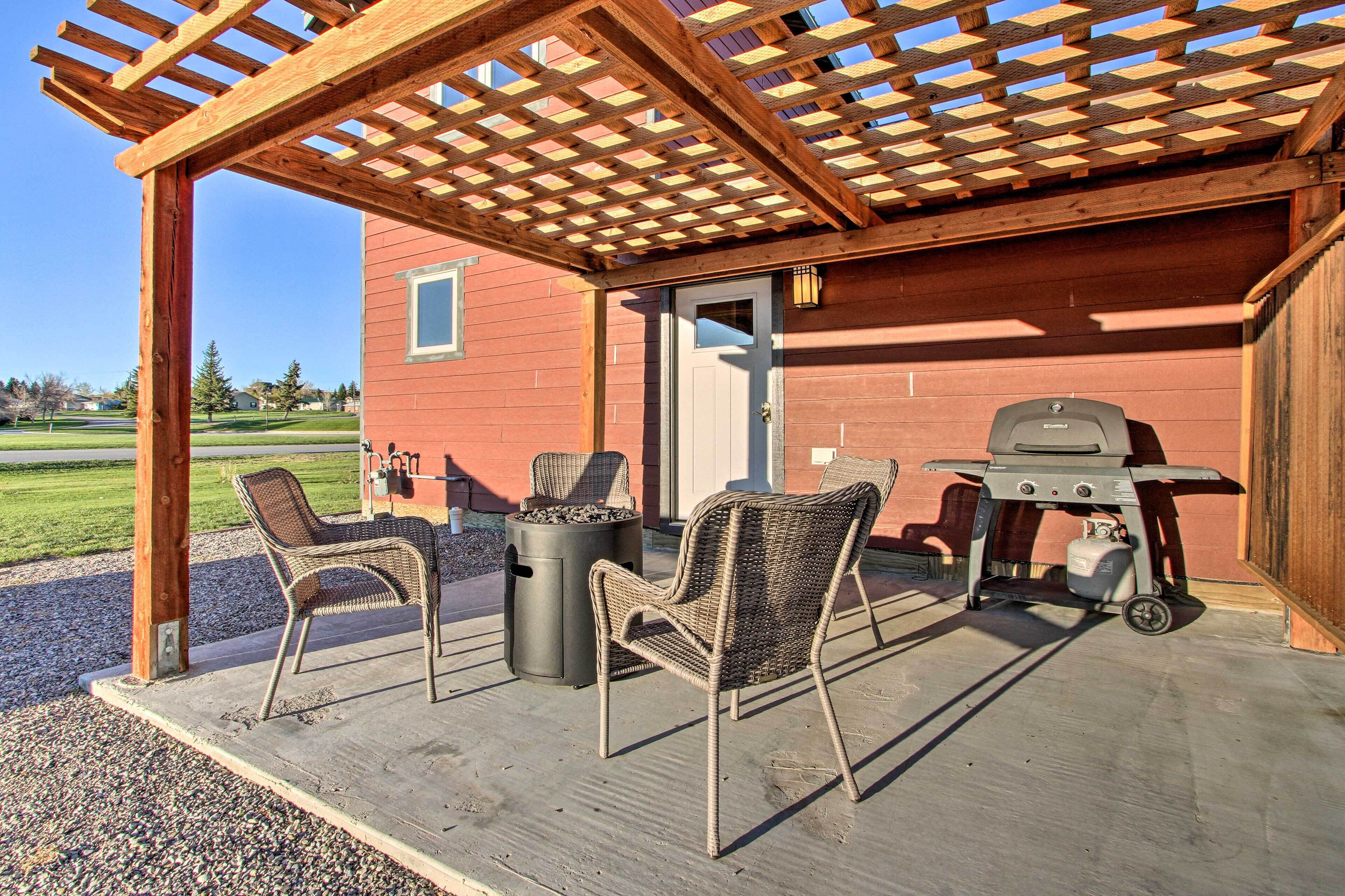Eine Terrass mit Holz-Pergola, zwei Korbstühlen, einem Grill und einem Mülleimer.