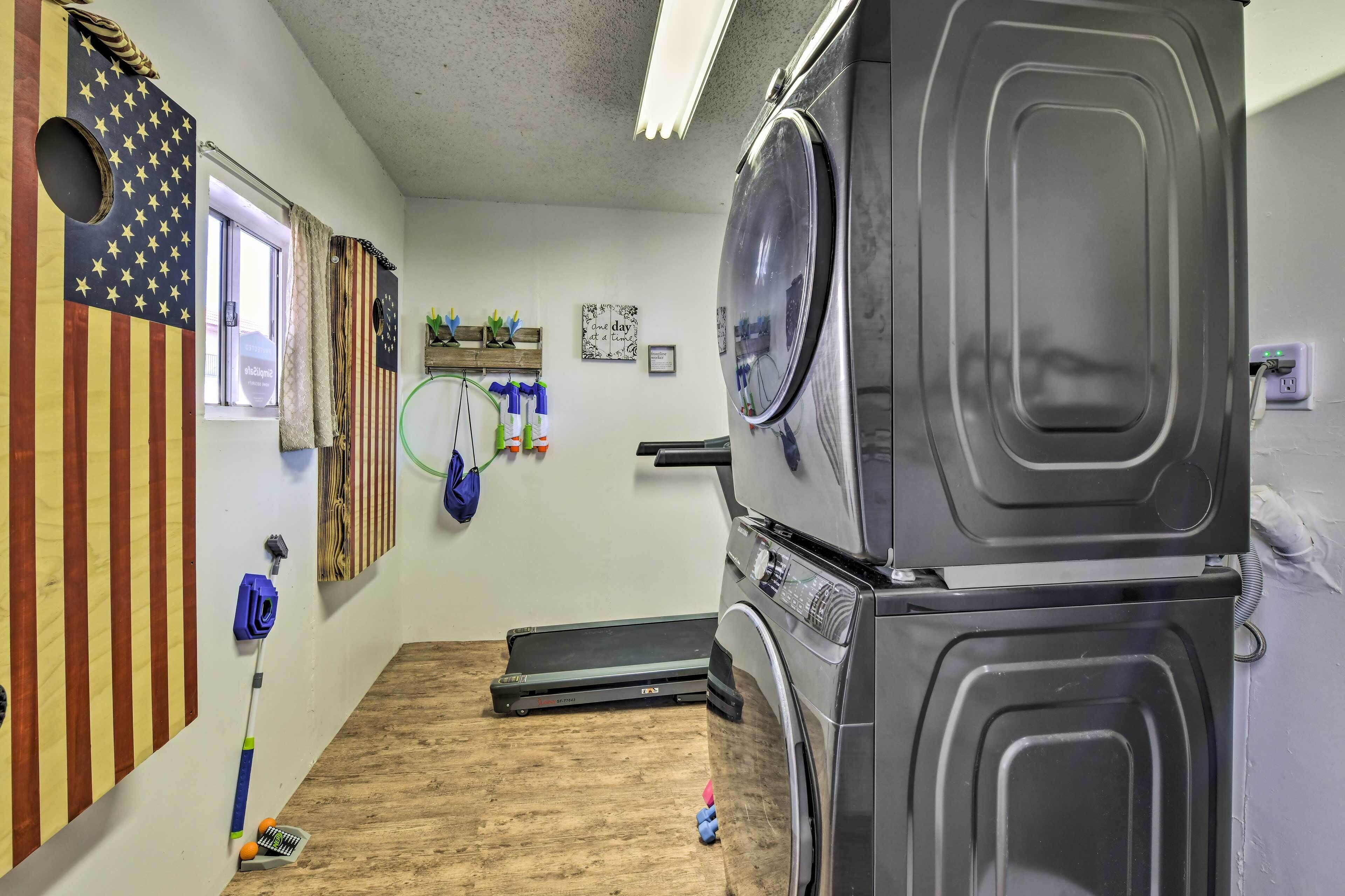 A laundry room with stacked washers and dryers, a window with curtains, and a treadmill.