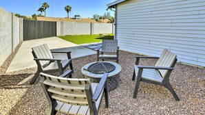Um pátio externo com quatro cadeiras Adirondack, um poço de fogo redondo e piso de concreto.