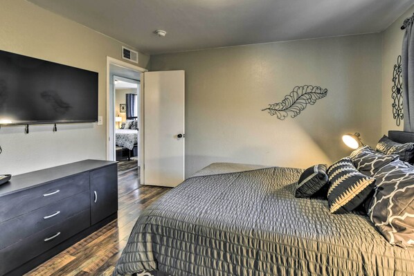 A bedroom with a bed, a dresser, a flat-screen TV, and a decorative leaf wall art.