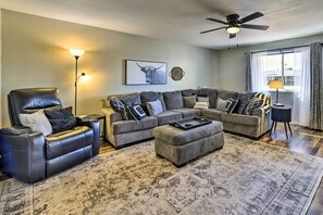 A living room with a leather chair, grey sofas, a patterned rug, a ceiling fan, and a framed picture on the wall.