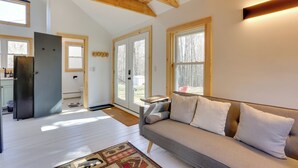 A modern living room with a grey sofa, wooden beams, and large windows. - Cozy Catskills Tiny Home ~ 3 Mi to Bethel Woods! (Swan Lake)