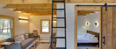 Une pièce chaleureuse avec un lit en mezzanine, un canapé, une échelle et une grande fenêtre.