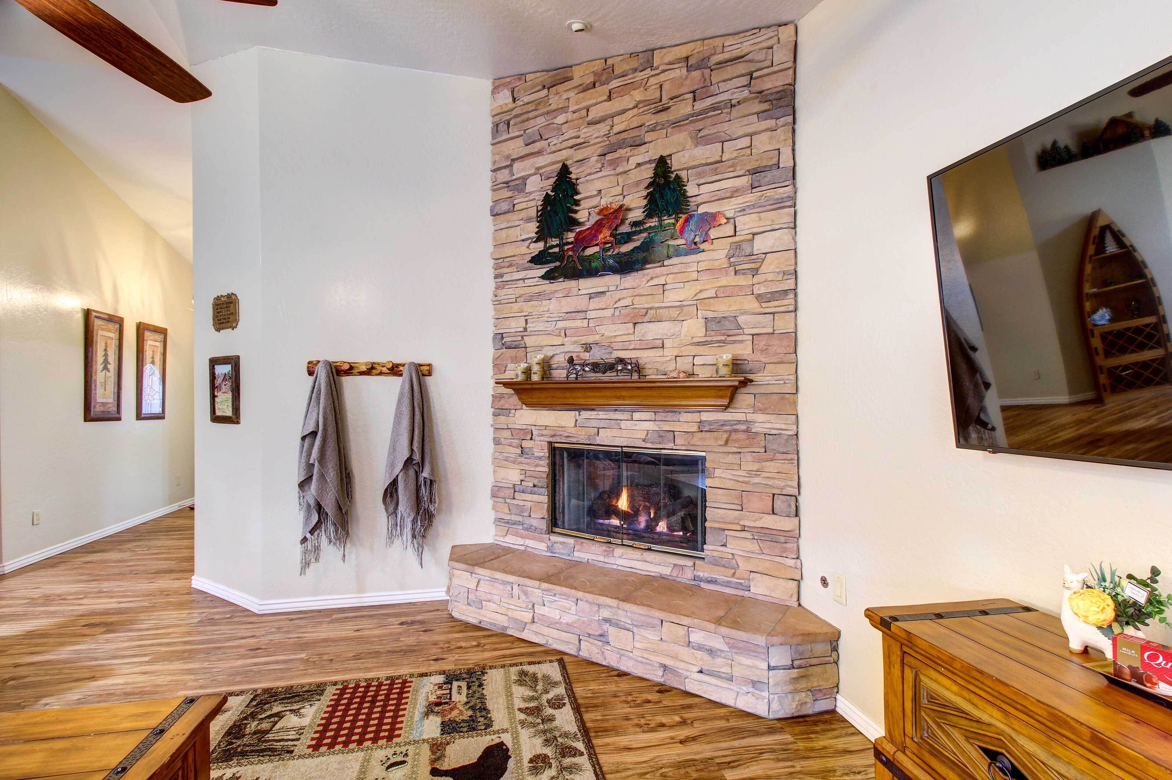 A living room with a stone fireplace, wooden flooring, and a mounted TV.