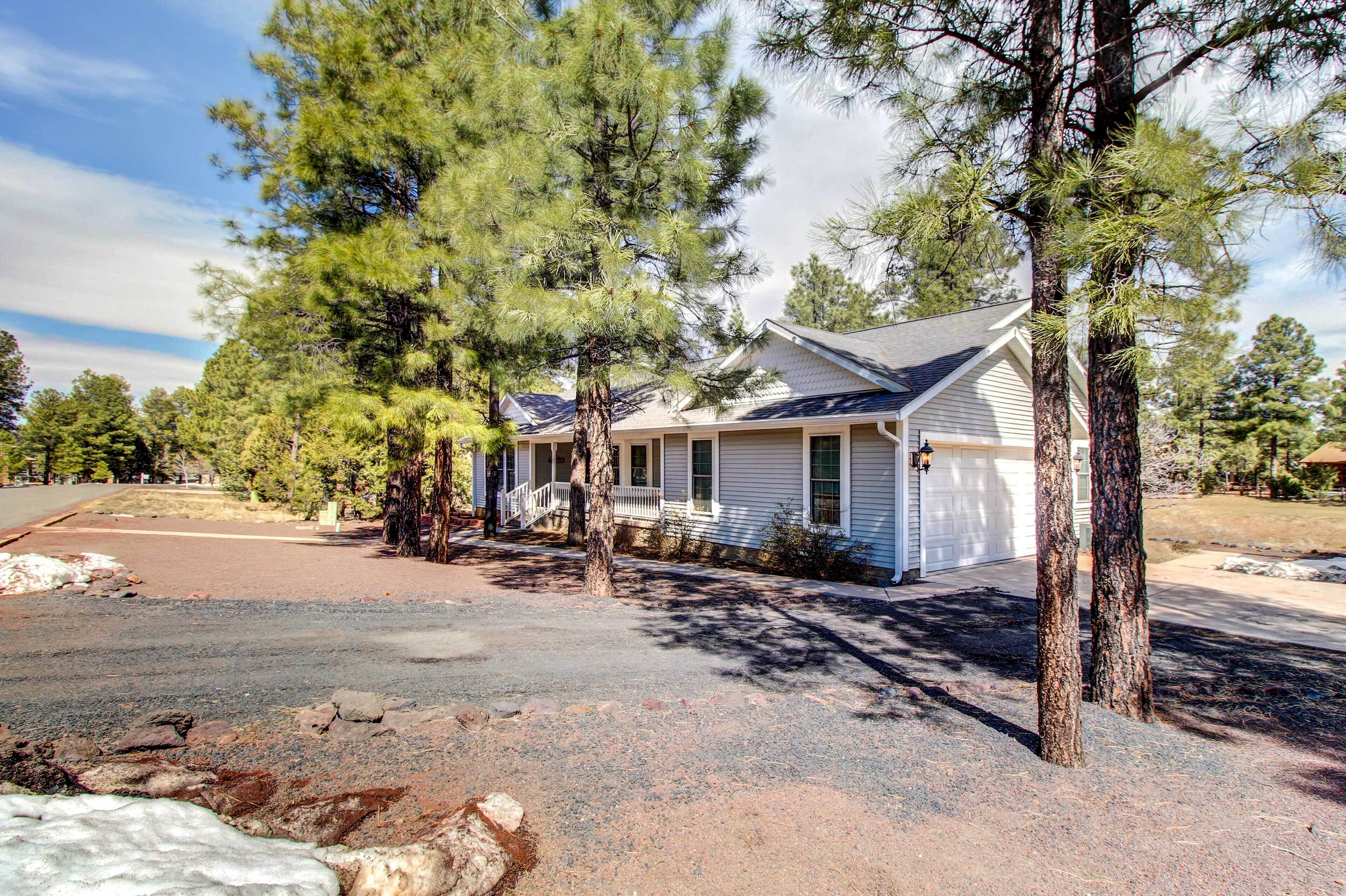 A two-story house with a covered porch and a garage, surrounded by pine trees.