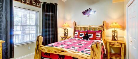 A bedroom with a wooden bed frame, a ceiling fan, two bedside lamps, a window with blinds, and a wall decoration.