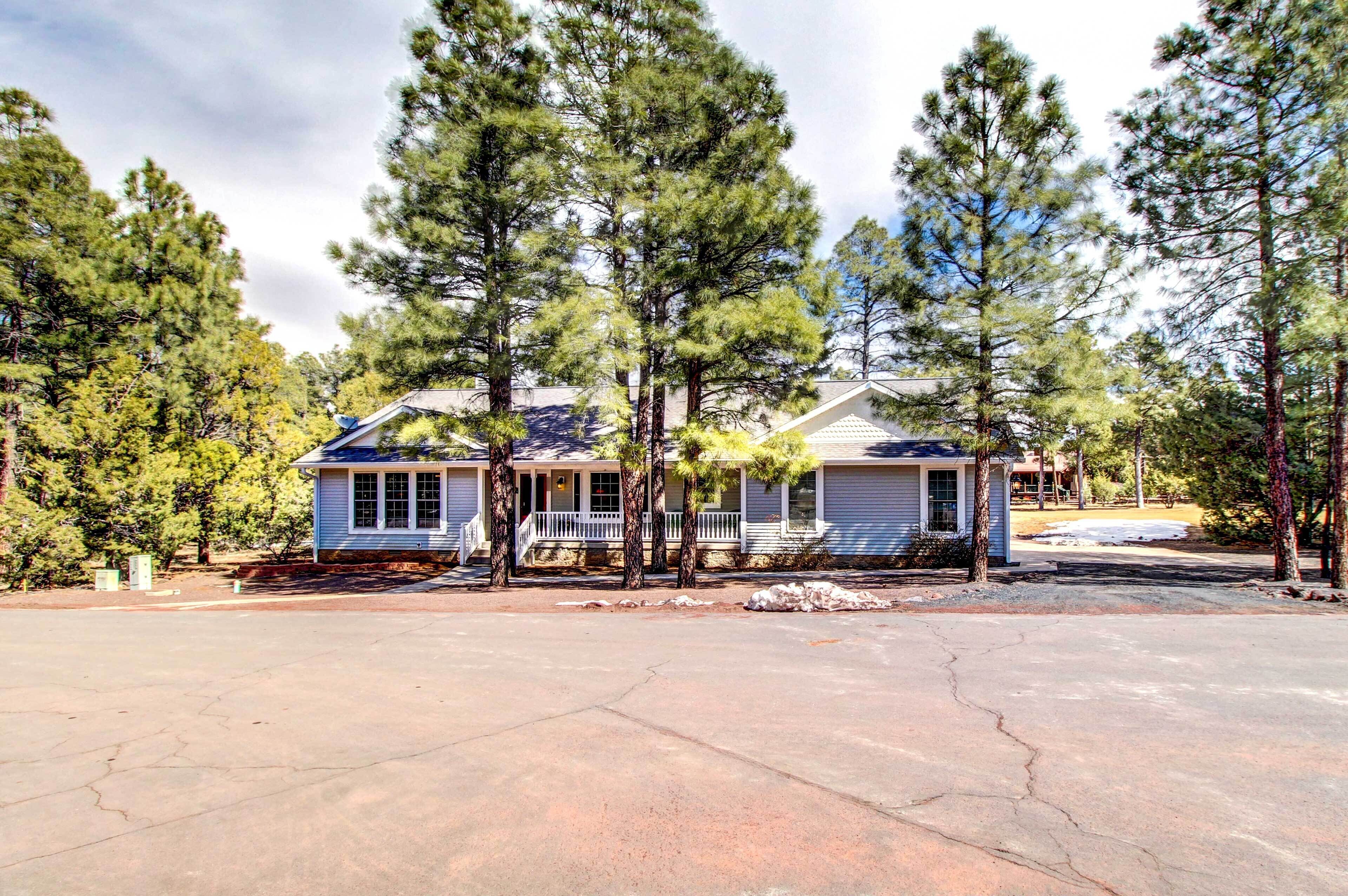 A two-story house with a porch, surrounded by tall pine trees.