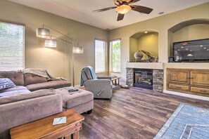A living room with a sectional sofa, a gray armchair, a wooden coffee table, a fireplace, and a flat-screen TV mounted above it. - Pool Table, Yard & Grill: Luxe Queen Creek Escape (Queen Creek)