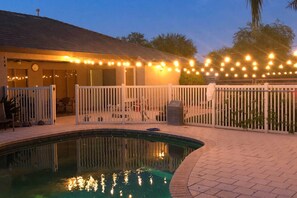 A swimming pool with a white fence, a covered patio area, and string lights. - Pool Table, Yard & Grill: Luxe Queen Creek Escape (Queen Creek)