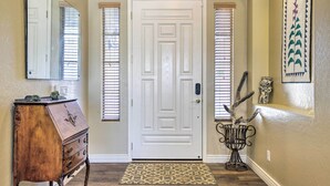 Un couloir avec une porte blanche, une commode en bois, un tapis à motifs et un élément décoratif fixé au mur.