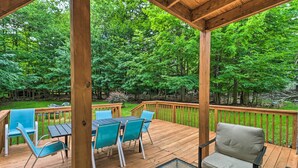 A wooden deck with outdoor furniture, surrounded by lush greenery. - Spacious Tobyhanna Family Home: Pool/beach Access! (Tobyhanna)